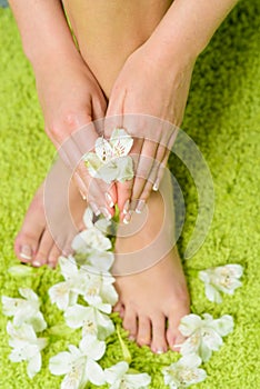 Beautiful feet with pedicure and flowers at green background