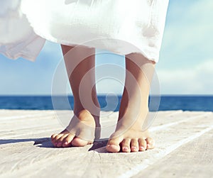 Beautiful feet of a woman in white dress on a wooden pier. Sea