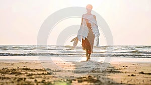 Beautiful female angel walking barefoot toward the sea at sunset.