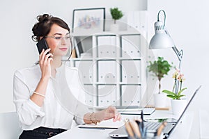 Beautiful female assistant calling using cellphone. Young office worker speaking on the mobile phone having business