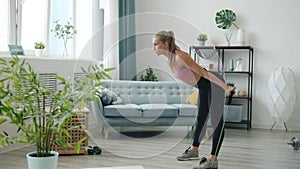 Beautiful female athlete doing exercises with resistance band training arms and body indoors at home