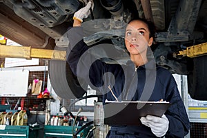 Beautiful female auto mechanic checking wheel tires in garage, car service technician woman repairing customer car at automobile