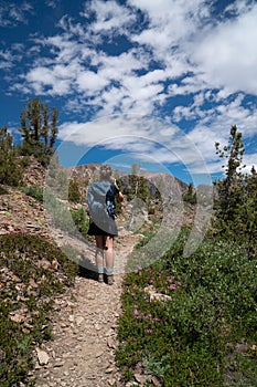 Beautiful female backpacker hiker takes photos along the trail in California`s eastern sierra nevada along 20 Lakes Basin Hike on