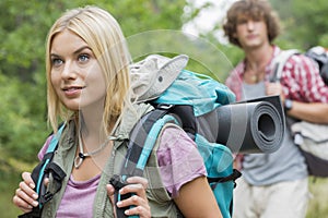 Beautiful female backpacker looking away with man in background at forest