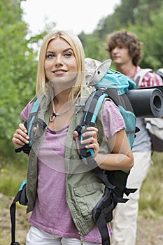 Beautiful female backpacker looking away with man standing in background at forest