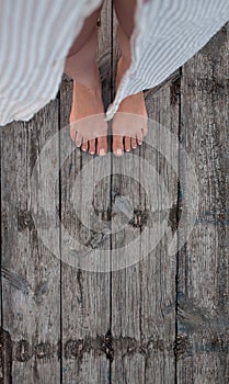 Beautiful female bare bare tanned legs with pink pedicure on wooden beach flooring. Top view, copy space