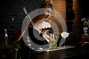 Beautiful female bartender professionally pours blue drink from jigger into cup. photo