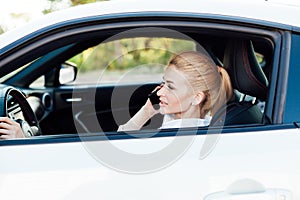 Beautiful female blonde driver talking smartphone behind the wheel of car