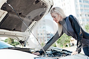 Beautiful female blonde mechanic looks engine under the hood of the car