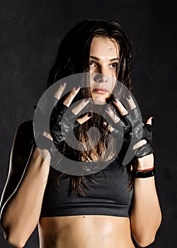 Beautiful female boxer or mma fighter wearing black gloves on a dark background