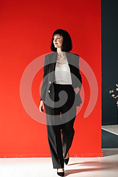 Beautiful female brunette business woman CEO in a black suit, isolated on red background, standing confidently with arms