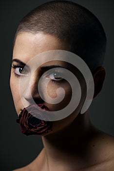 Beautiful female cancer patient with shaved head and rose in her mouth. Cancer taboo, equality and discrimination.