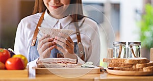 A beautiful female chef cooking and eating a whole wheat ham cheese sandwich in kitchen