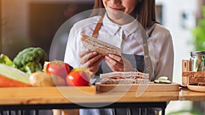 A beautiful female chef cooking and eating a whole wheat ham cheese sandwich in kitchen