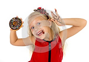 Beautiful female child with blue eyes in cute red dress eating chocolate donut with syrup stains