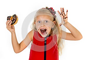 Beautiful female child with blue eyes in cute red dress eating chocolate donut with syrup stains