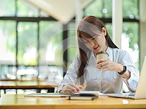 Beautiful female college student, businesswoman, doing an assignment while drinking coffee at cafe