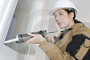 beautiful female construction worker using caulking gun