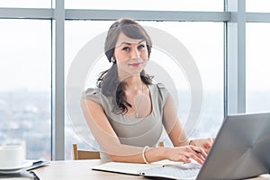 Beautiful female copywriter sitting in office, typing new article, working with text, using laptop at workplace. photo