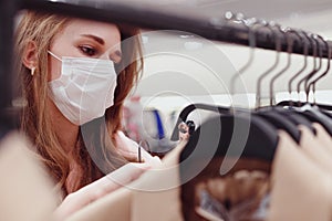 Beautiful female customer in protective face mask shopping in clothing store