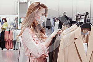 Beautiful female customer in protective face mask shopping in clothing store