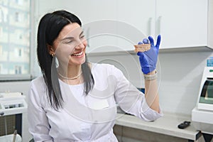 Beautiful female dentist doctor, dental technician smiling, showing at camera a gypsum mold of human upper jaw model