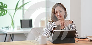 Beautiful female designer editing her project with tablet and smiling at the camera in comfortable workplace