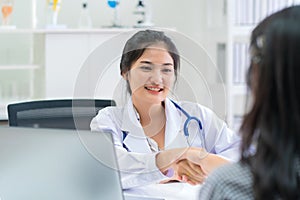 Beautiful female doctor at medical office wearing stethoscope and lab coat shaking hands with patient and smiling in hospital