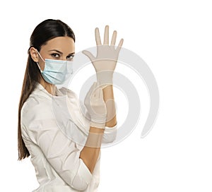 Beautiful female doctor or nurse wearing protective mask and latex or rubber gloves on white background with copyspace
