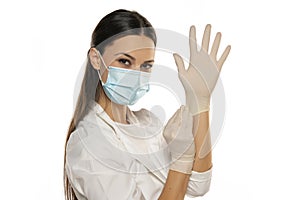 Beautiful female doctor or nurse wearing protective mask and latex or rubber gloves on white background with copyspace