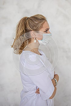 Beautiful female doctor or nurse wearing protective mask and medical gown posing on white background. Healthcare concept