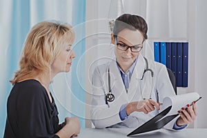 Beautiful female doctor showing medical records to her senior patient