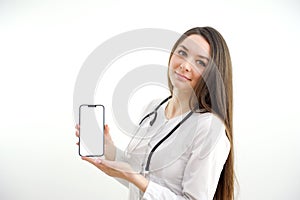 Beautiful female doctor smiling and showing a blank smart phone screen isolated on a white background. Portrait of happy