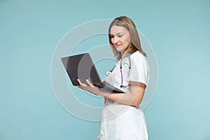 Beautiful female doctor with a stethoscope and a laptop, on a blue background. Online consultation. Copy paste