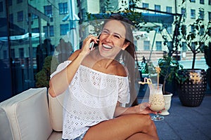 Beautiful female enjoying her cocktail on open terrace and chatting on the phone