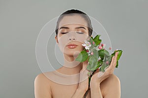 Beautiful female face with flowers. Spring woman relaxing on grey background, studio portrait