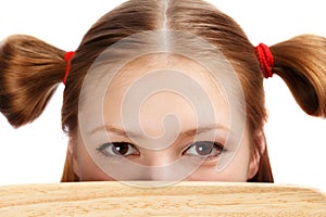 Beautiful female face with funny ponytails tied by red scrunchies hidden behind wooden cutting board