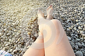 Beautiful female feet on pebbles on the beach on a Sunny summer day