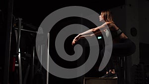 Beautiful female fitness athlete performs box jumps in a dark gym wearing black sports top and short tights with face