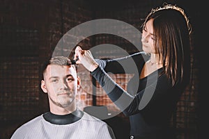 Beautiful female hairdresser cutting client`s hair with scissors in a barber shop. Concept of advertising and hairdressing