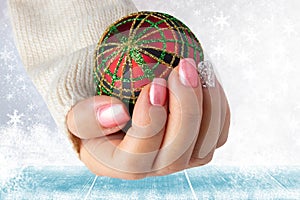 Beautiful female hand with christmas nail design. Hand with elegant pink nail manicure holding a red christmas decoration ball. S