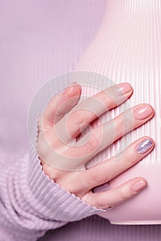 Beautiful female hand holding pink vase on the pale violet background. Manicure with pink color nail polish with shiny design,