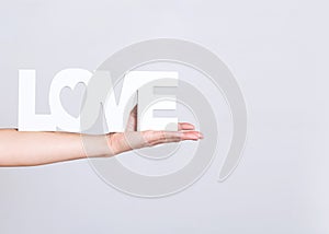 Beautiful female hand holding the word love, white color on light grey background,