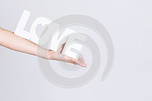 Beautiful female hand holding the word love, white color on light grey background,