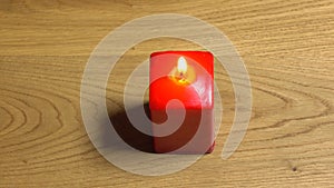 Beautiful female hand lighing up red square candle on wooden table. Romantic evening or romance concept. 4K video, top