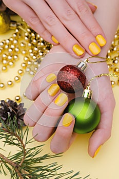 Beautiful female hand with yellow nail design. Christmas manicure.