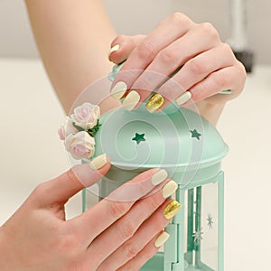 Beautiful female hands with a manicure and a lamp-candlestick on a light background. Yellow with gold nails
