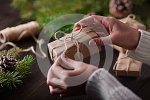 Beautiful female hands are packed Christmas gift in brown kraft paper.