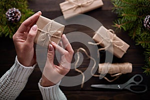 Beautiful female hands are packed Christmas gift in brown kraft paper.