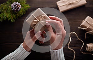 Beautiful female hands are packed Christmas gift in brown kraft paper.